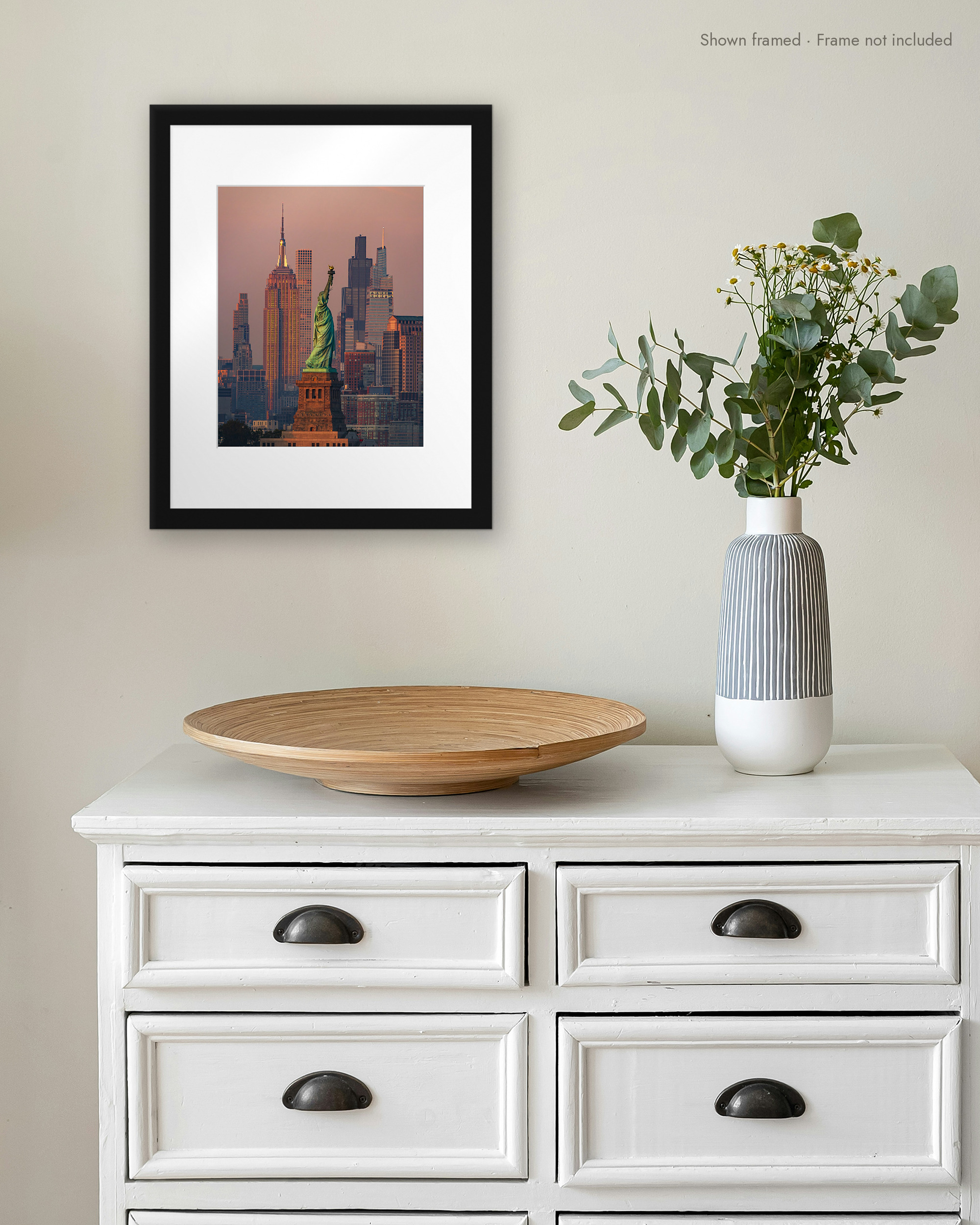 Lady Liberty Sunset print in a white mat and black frame on a wall above a white dresser