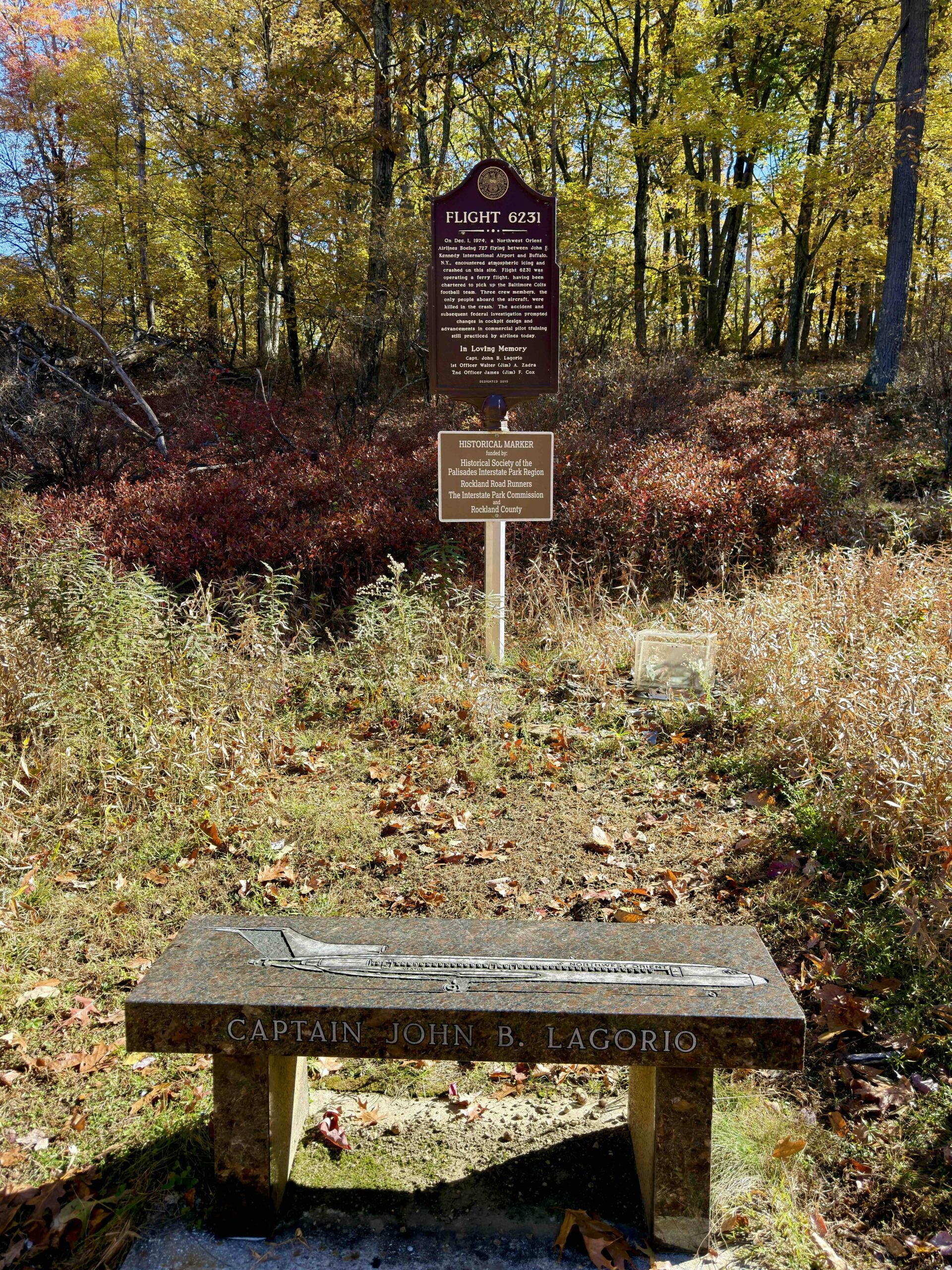 Flight 6231 historical marker in the woods, with a granite memorial bench for Captain John B. Lagorio in the foreground