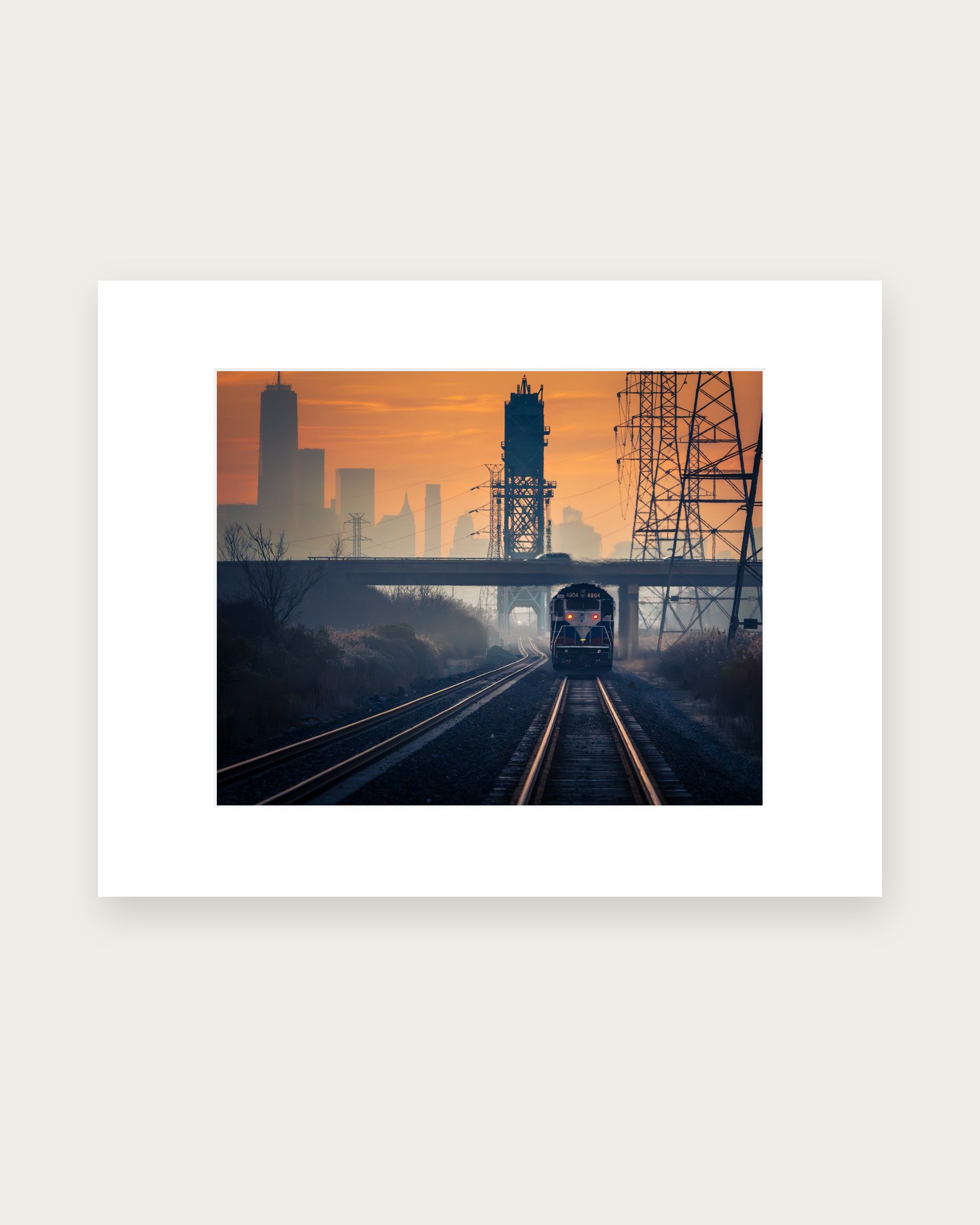 Matted photographic print of a train crossing the New Jersey Meadowlands at dawn, with Manhattan in the distance.