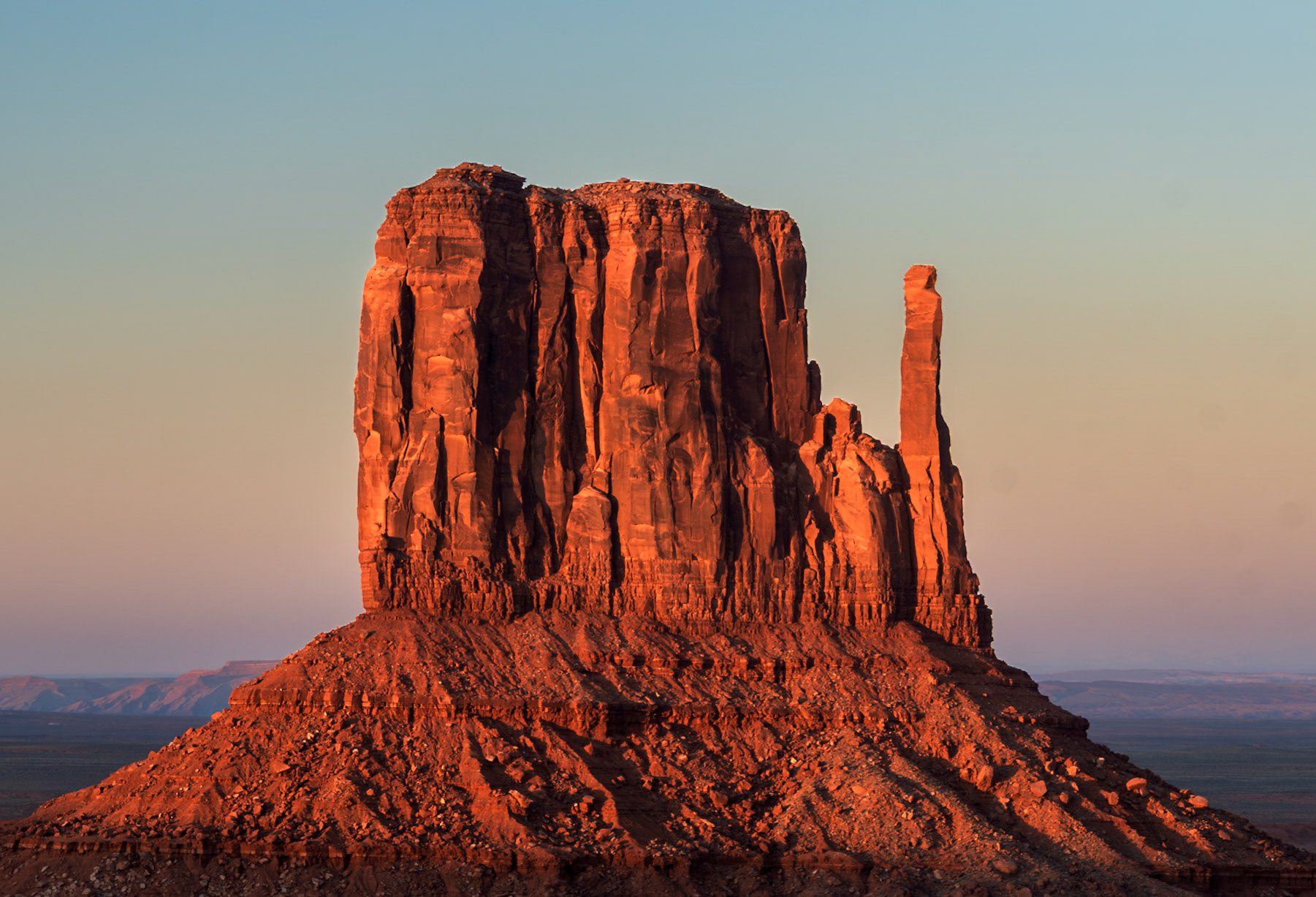 A sandstone butte in Monument Valley glowing red at sunset