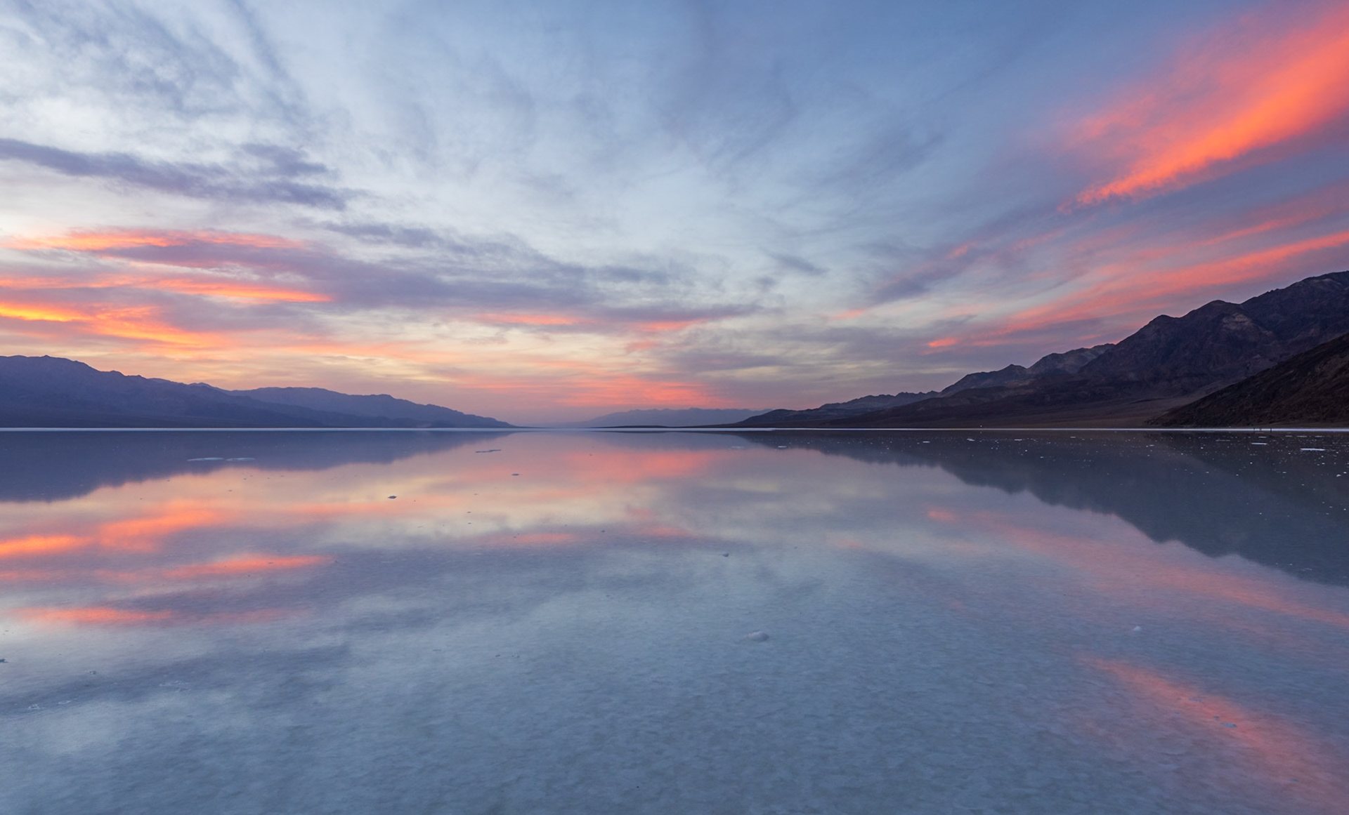 Sunset colors mirrored in a thin sheet of water on a desert salt flat