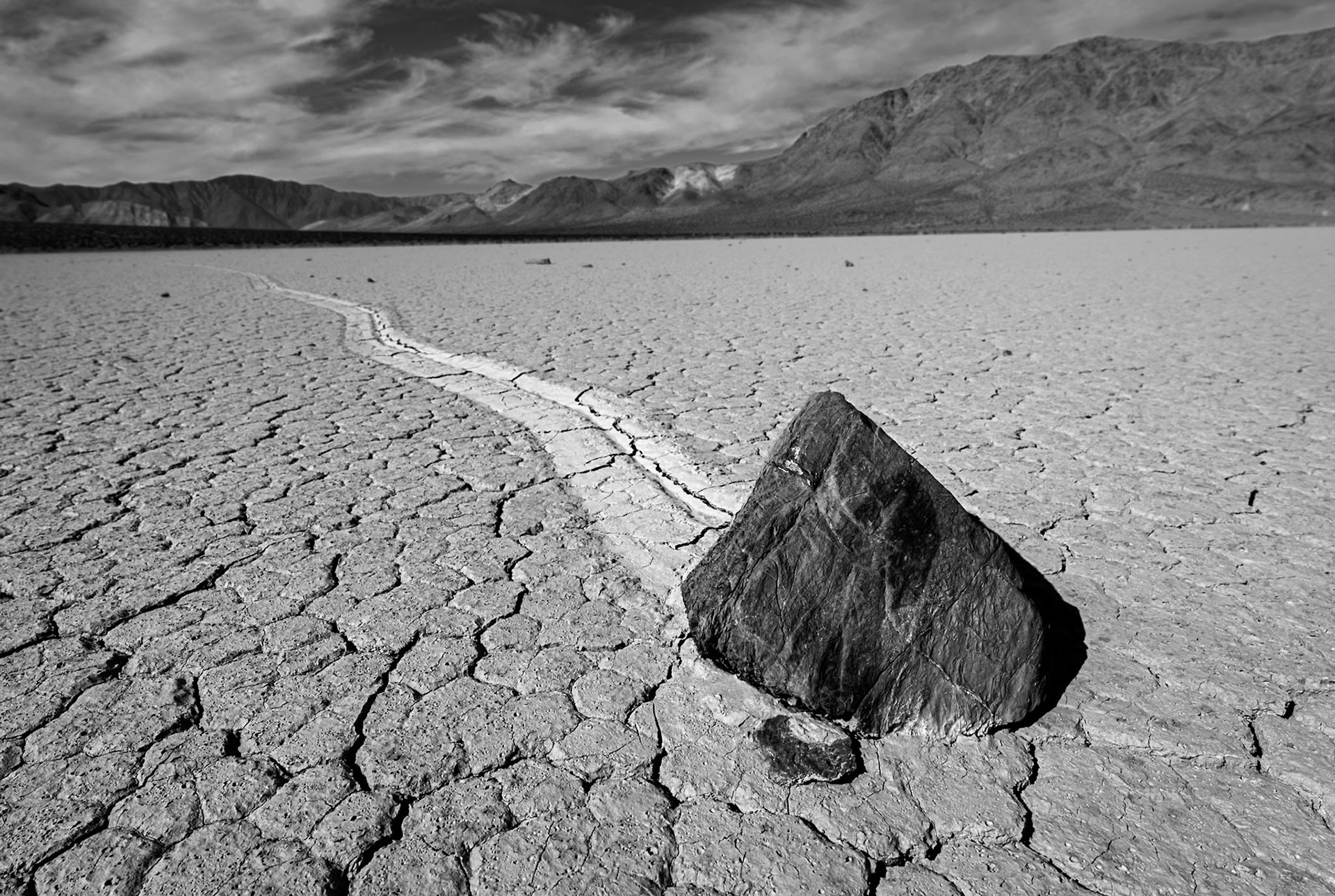A sailing stone and its long track on the cracked Racetrack Playa in Death Valley, in black and white