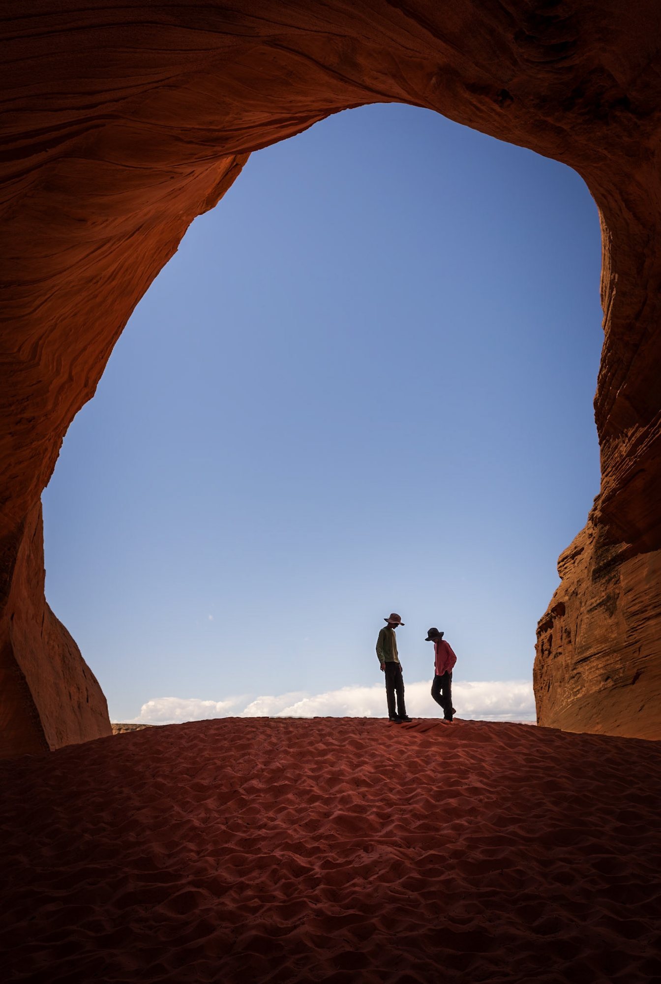 Two people silhouetted in the mouth of a sandstone cave against blue sky