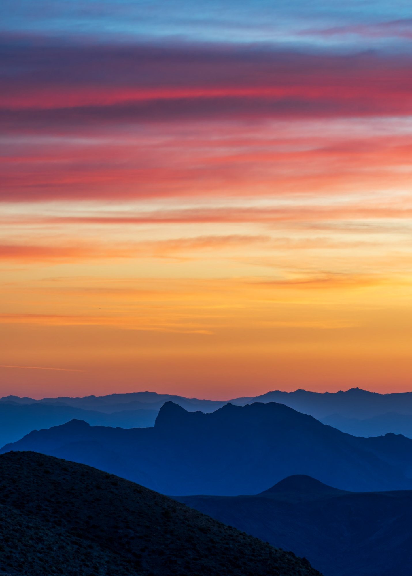 Blue desert mountain ridges beneath a vivid orange and pink sky