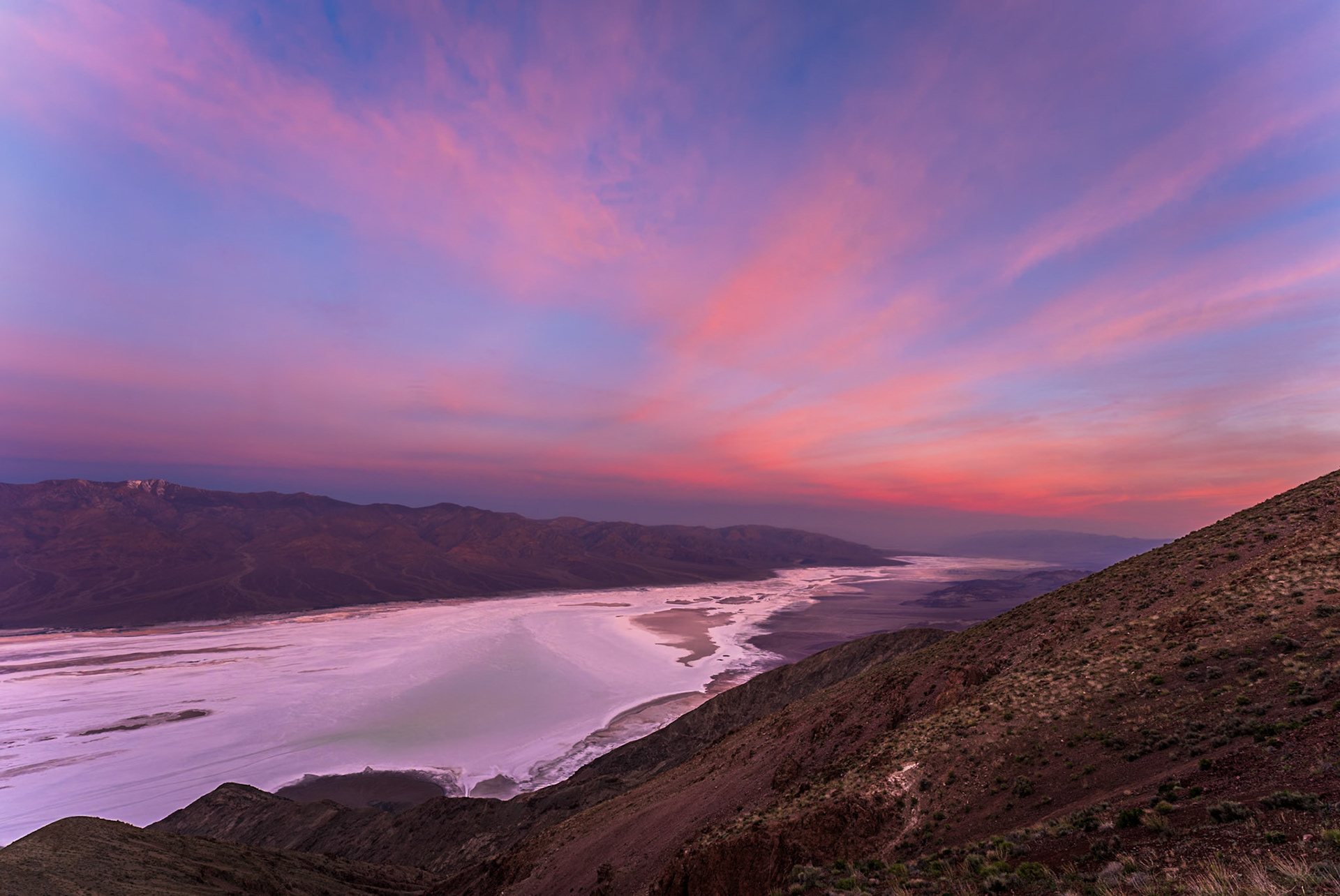 A pink sunset over a desert salt flat seen from a high ridge