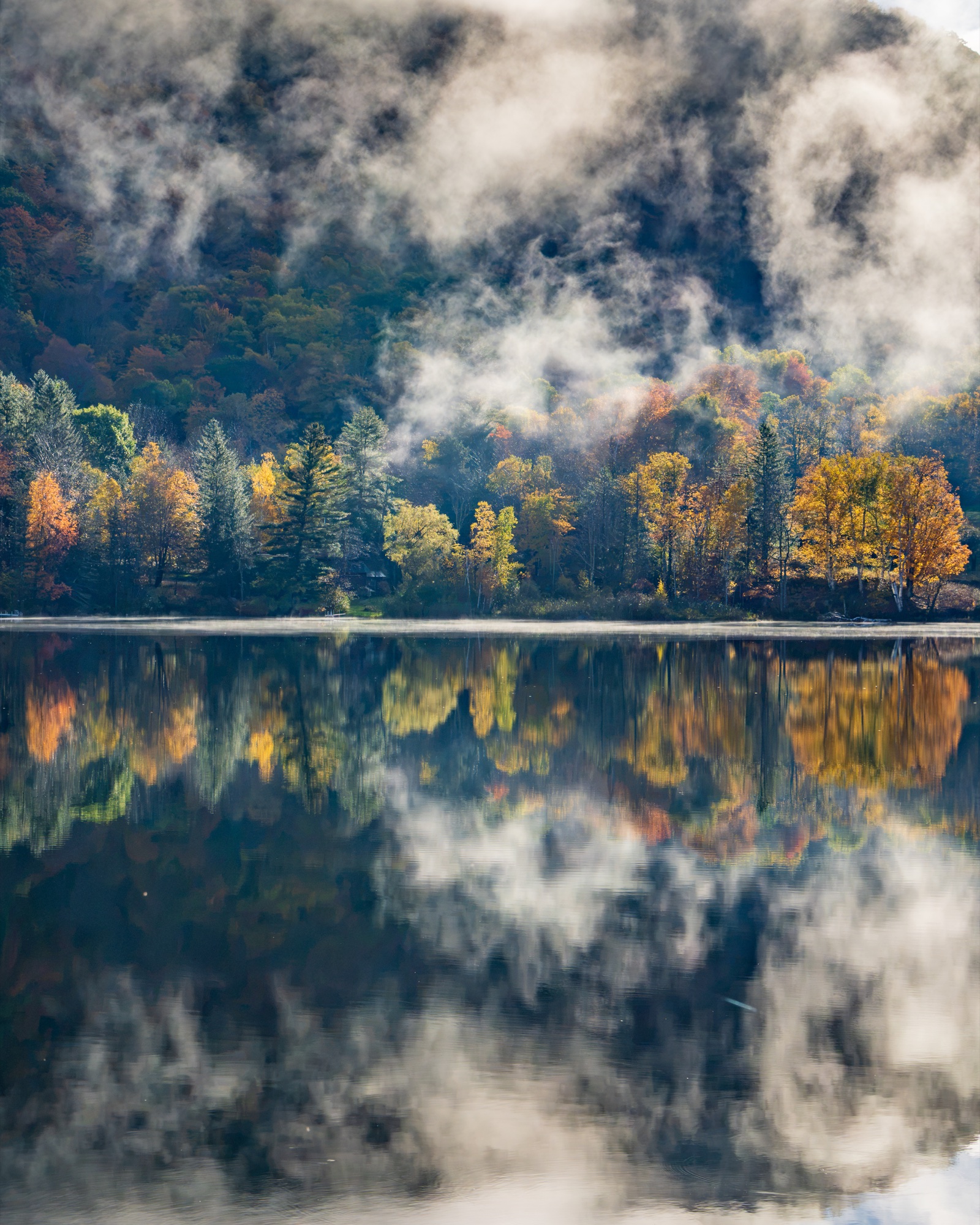 Morning fog drifting through autumn trees and reflected in a lake along Route 100