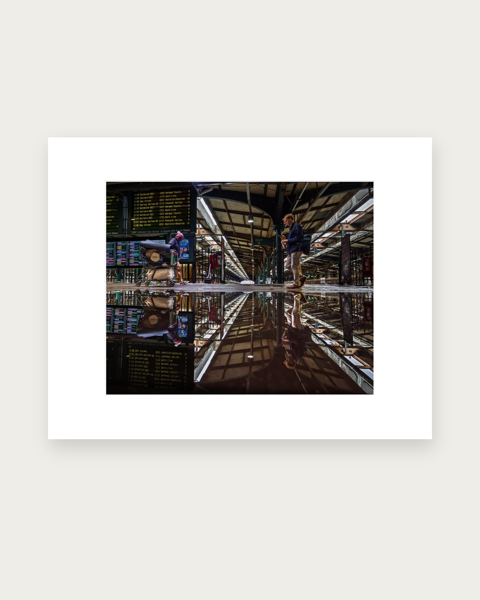 Matted photographic print of Hoboken Terminal’s train shed reflected upside down in a rain puddle, with two travelers walking in opposite directions.