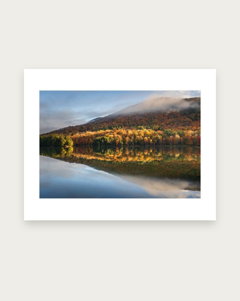 Matted photographic print of peak fall foliage and a lifting cloud bank reflected in Woodward Reservoir along Route 100 in Vermont.